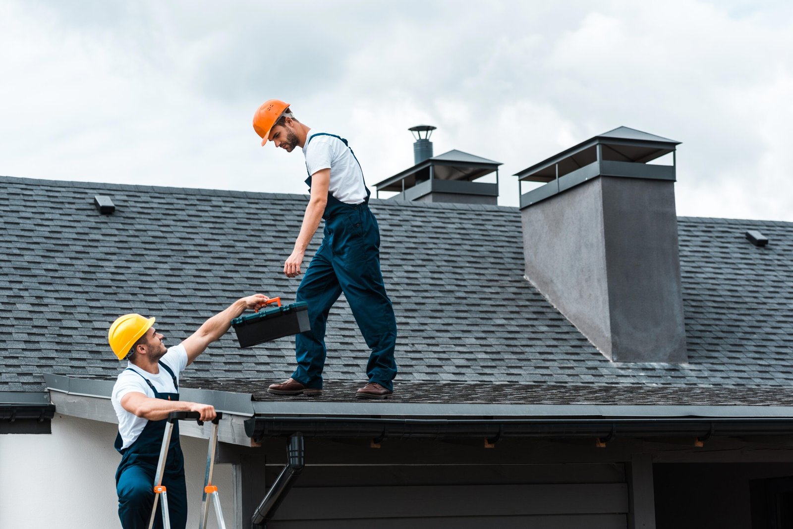 handyman in helmet giving toolbox to handsome colleague standing